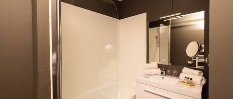 Une salle de bain moderne avec une douche à parois de verre, un meuble-lavabo blanc avec un miroir et un porte-serviettes.