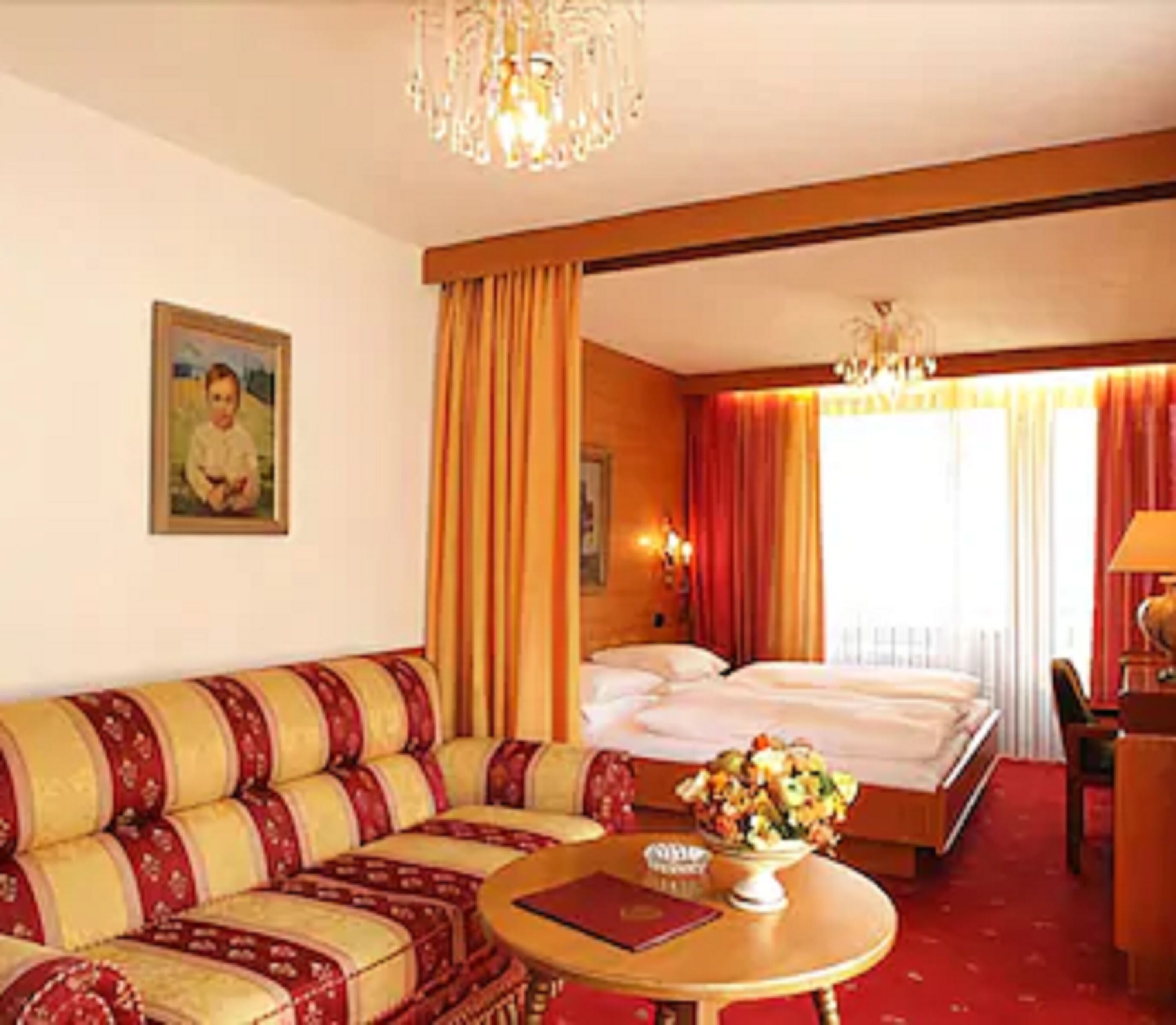 Ein Hotelzimmer mit einem Bett, einem Sofa, einem Esstisch mit Blumenvase und einem Bild an der Wand.