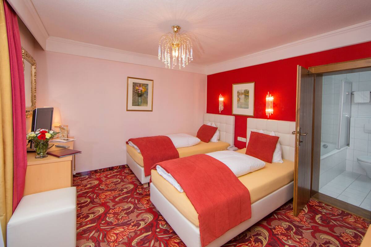 Ein Hotelzimmer mit zwei Betten, einem Schreibtisch mit Lampe und einer Dusche.