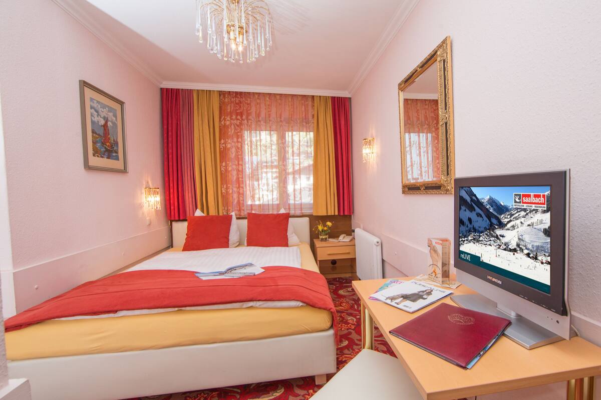Ein Hotelzimmer mit Bett, Schreibtisch mit Computer, Spiegel und Fenster mit Vorhängen.