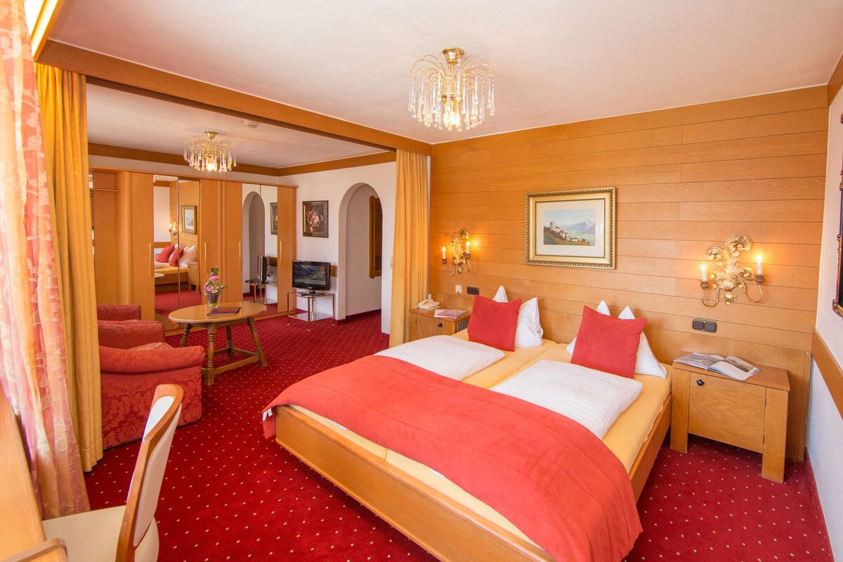 Ein Hotelzimmer mit einem großen Bett, zwei Nachttischen, einem Fernseher und einer Chandelüster.