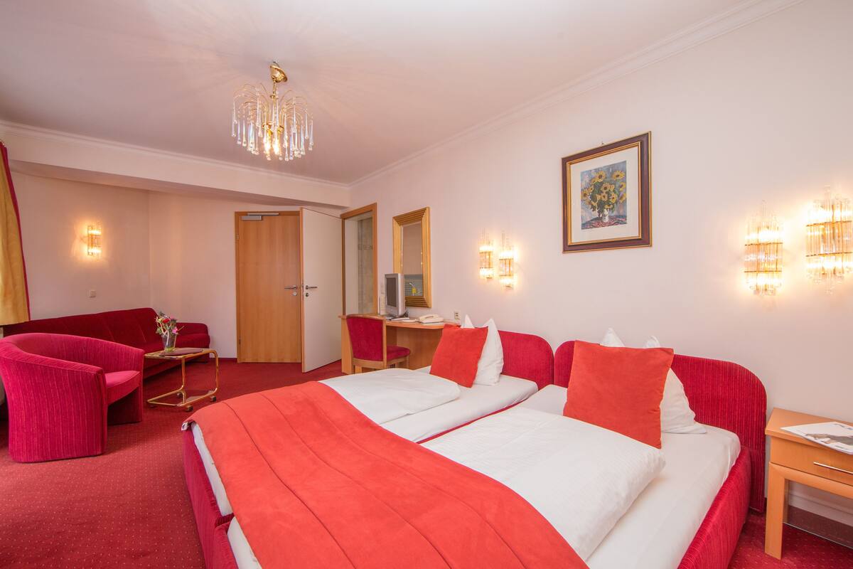 Ein Hotelzimmer mit einem großen Bett, zwei roten Sesseln, einem Schreibtisch mit Computer und einem Spiegel.