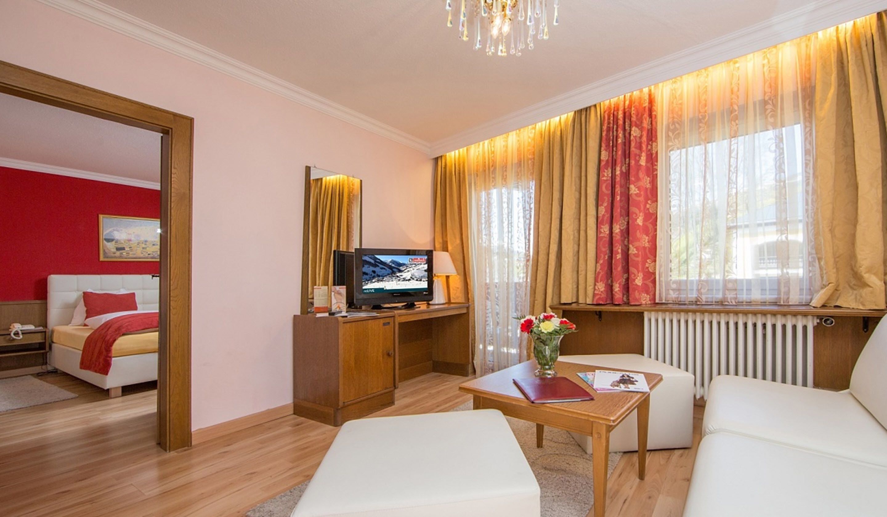 A hotel room with a bed, a TV, a small table with a vase of flowers, and a window with curtains.