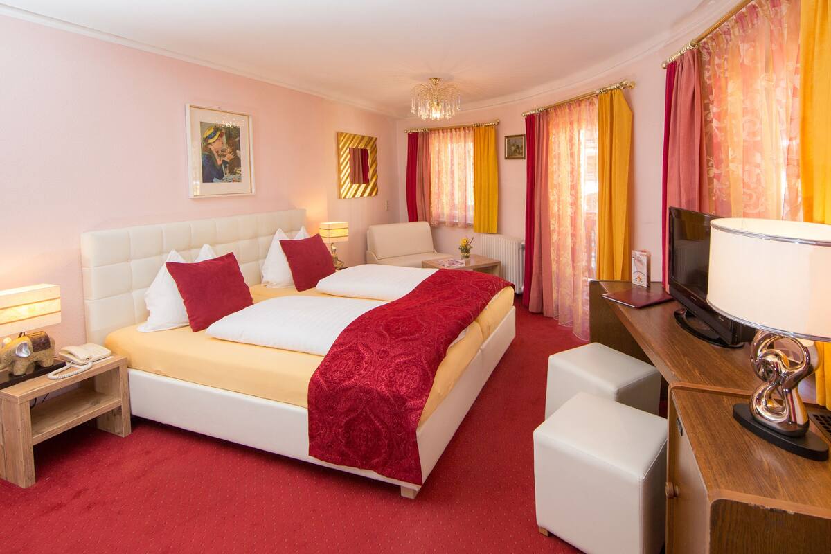 Ein Hotelzimmer mit einem großen Bett, zwei Nachttischen, einem Schreibtisch mit Fernseher und einem Sessel.
