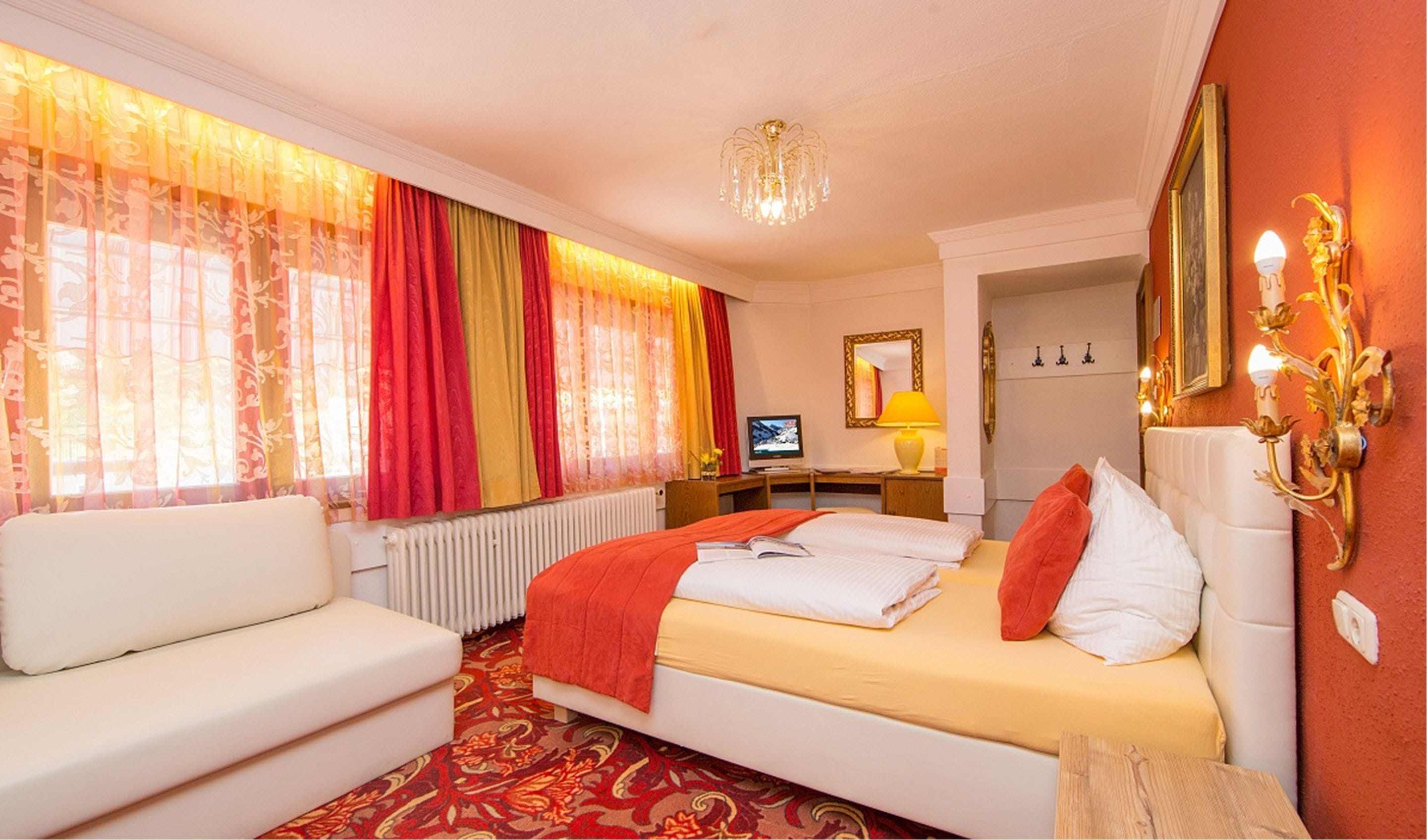 A hotel room with a bed, a sofa, a desk with a computer, and a TV.