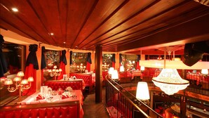 Un restaurante con asientos tapizados en rojo, candelabros y techo de madera.