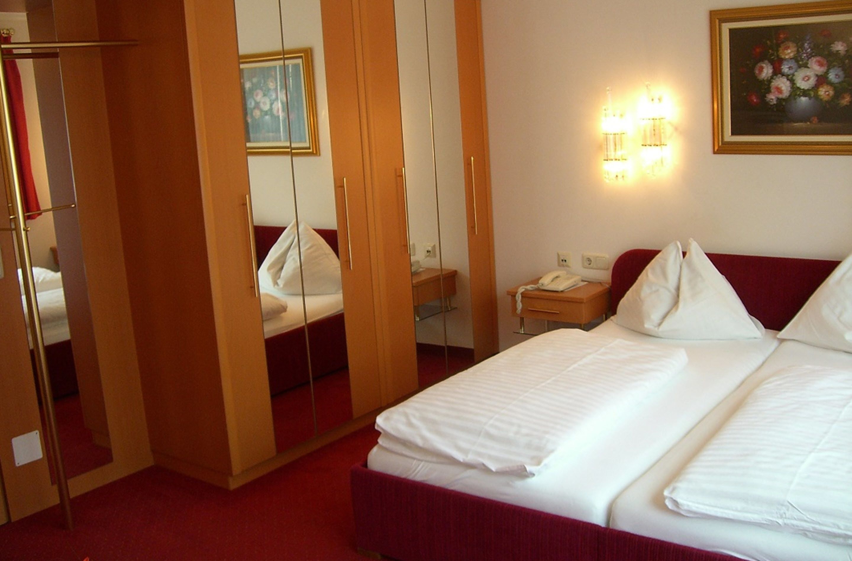 A hotel room with a bed, a nightstand, a mirror, and a painting on the wall.