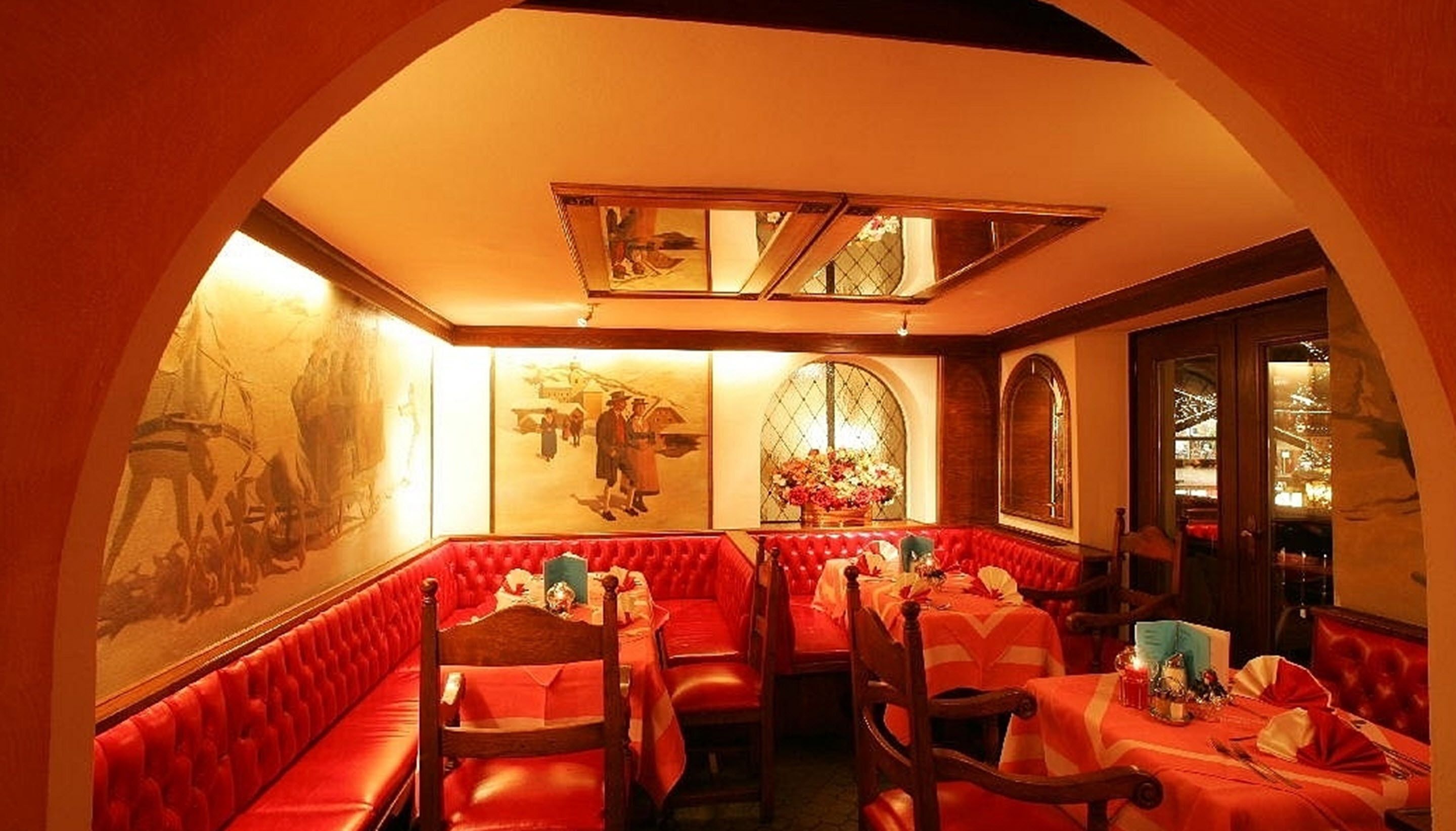 A restaurant with red upholstered booths, a high ceiling with a skylight, and artwork on the walls.