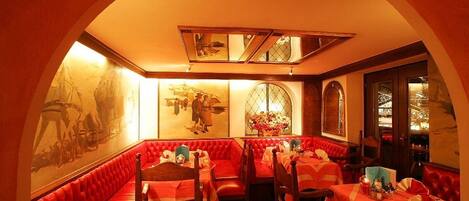 A restaurant with red upholstered booths, a high ceiling with a skylight, and artwork on the walls.