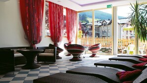 Una habitación con suelo de cuadros, muebles de mimbre, cortinas rojas y vistas a edificios tradicionales a través de amplias ventanas.