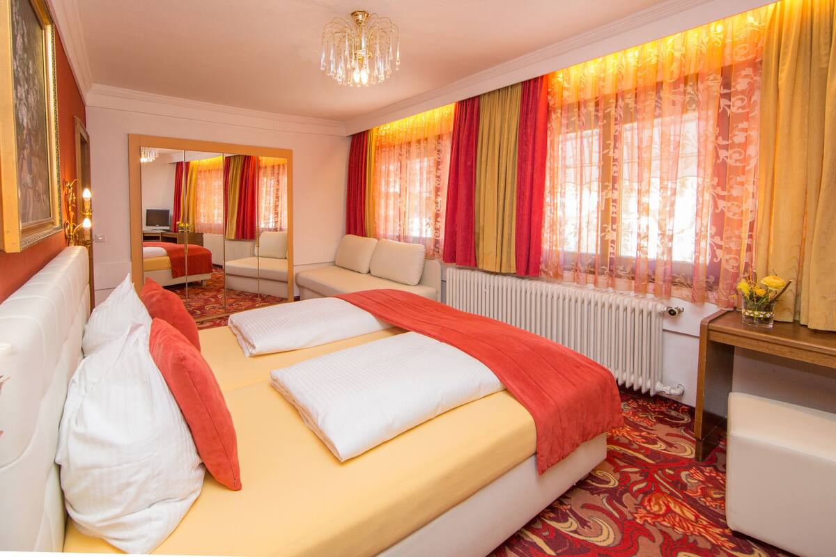 Ein Hotelzimmer mit einem großen Bett, einer Sitzecke, einem Spiegel und einem Fenster mit Vorhängen.