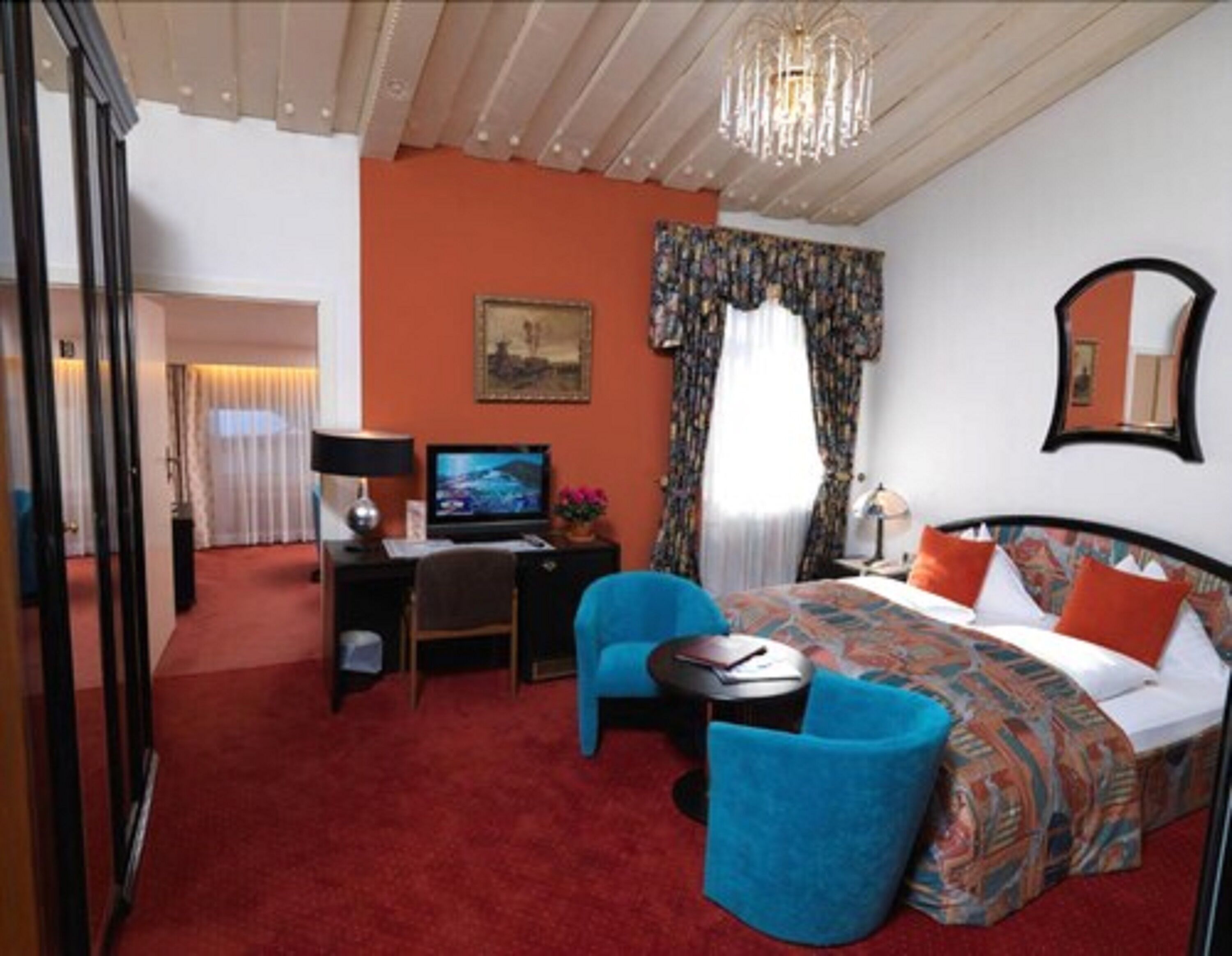 Ein Hotelzimmer mit einem Bett, einem Schreibtisch mit Computer, einem Sessel, einem Fernseher und einer Deckenleuchte.