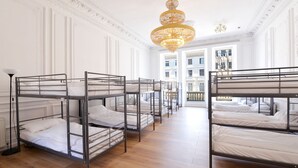 Habitación de hotel con literas, una araña y vistas de la ciudad a través de amplios ventanales.