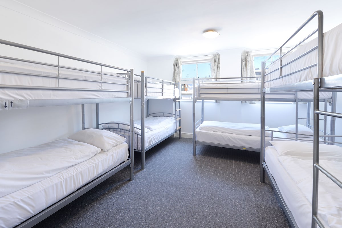 A room with bunk beds, a window with curtains, and a ceiling light.