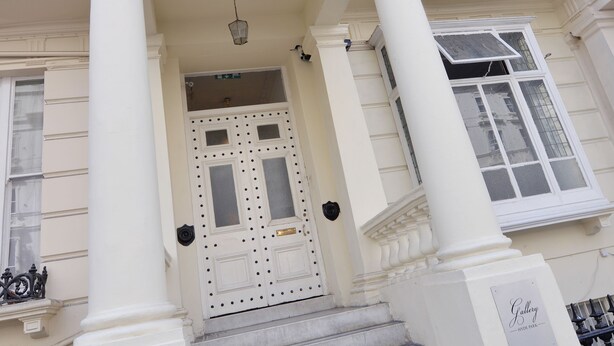 Un edificio con fachada clásica, una escalera que lleva a una puerta con diseño decorativo y un letrero que indica el número 23.