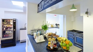 Una cocina con refrigerador, pileta, estufa y una mesada con alimentos y un cuenco de frutas.