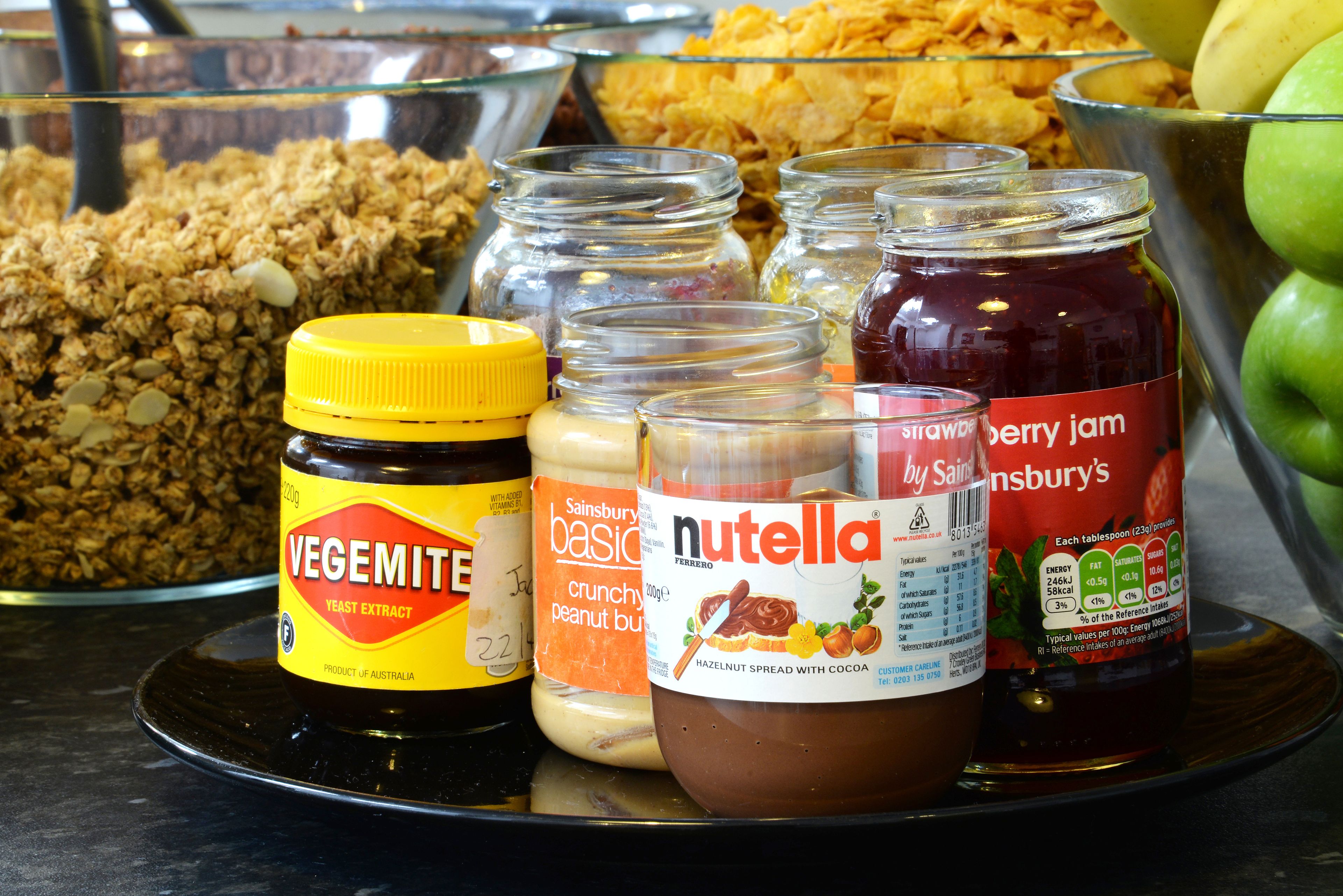 A variety of food items including jars of Vegemite, Sainsbury's basic crunchy peanut butter, Nutella, and strawberry jam.