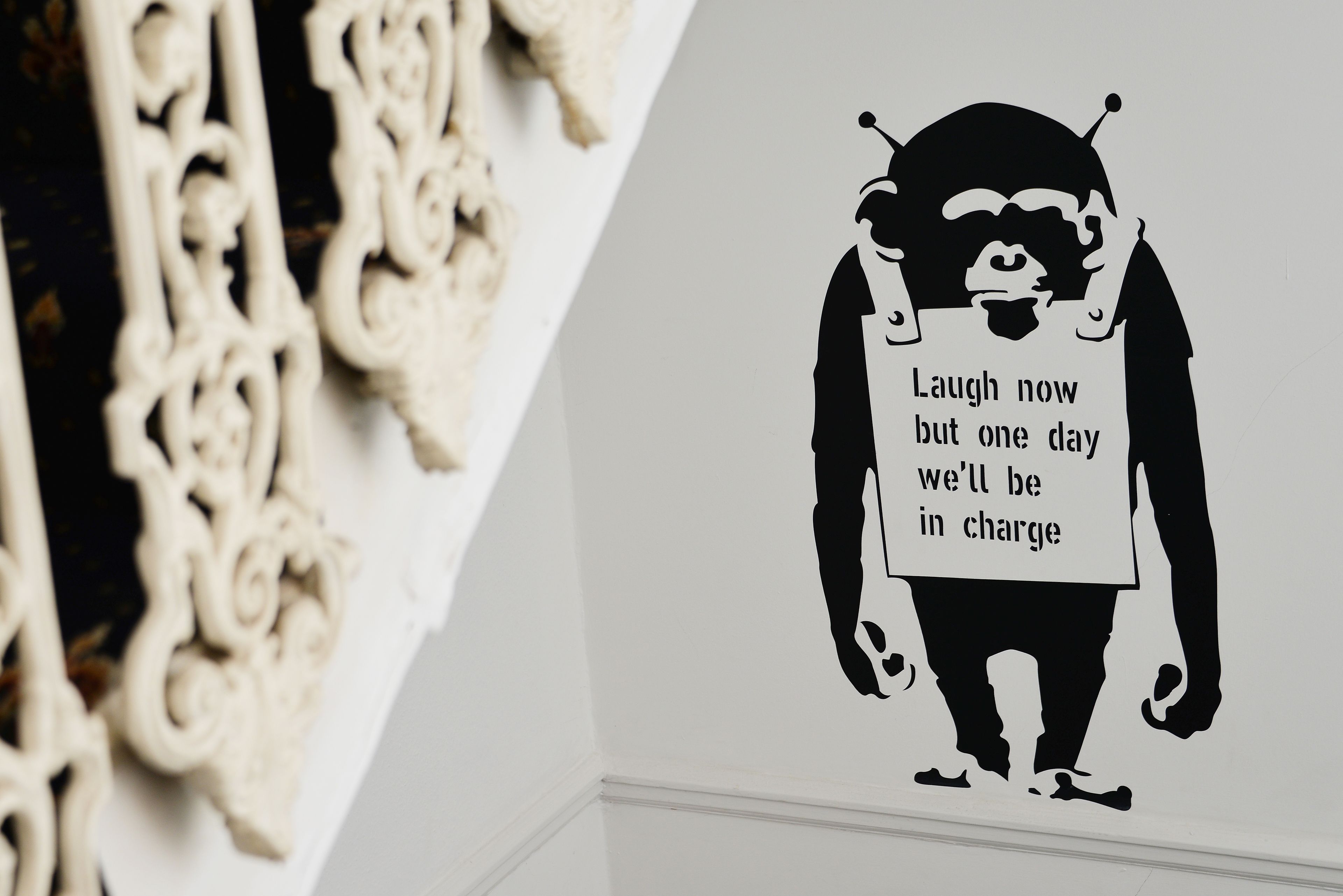 A wall with a black and white illustration of a gorilla holding a sign that says "Laugh now but one day we'll be in charge."