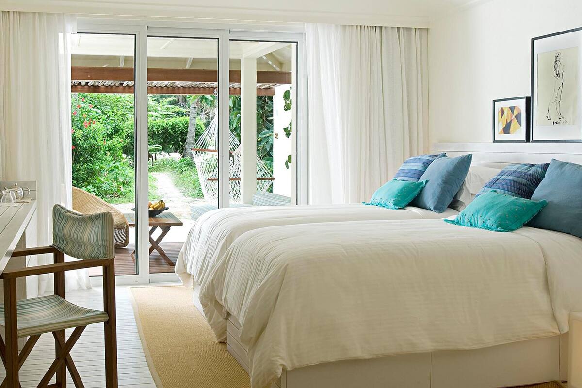 A bedroom with a bed, a desk with a chair, a TV, and a view of a garden through a sliding door.