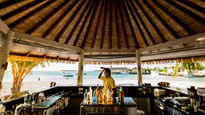 A beachside bar with a thatched roof, a bartender, and a view of the beach and ocean. - Holiday Inn Resort Kandooma Maldives by IHG (Kandooma)