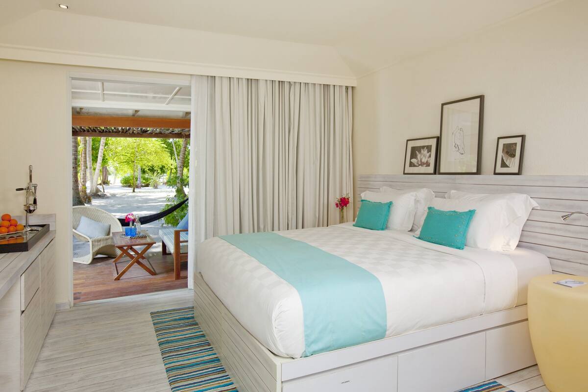 A bedroom with a large bed, a desk with a chair, and a view of a garden through a sliding door.