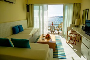 A hotel room with a sofa, a dining table with fruit, a TV, and a view of the sea. - Holiday Inn Resort Kandooma Maldives by IHG (Kandooma)