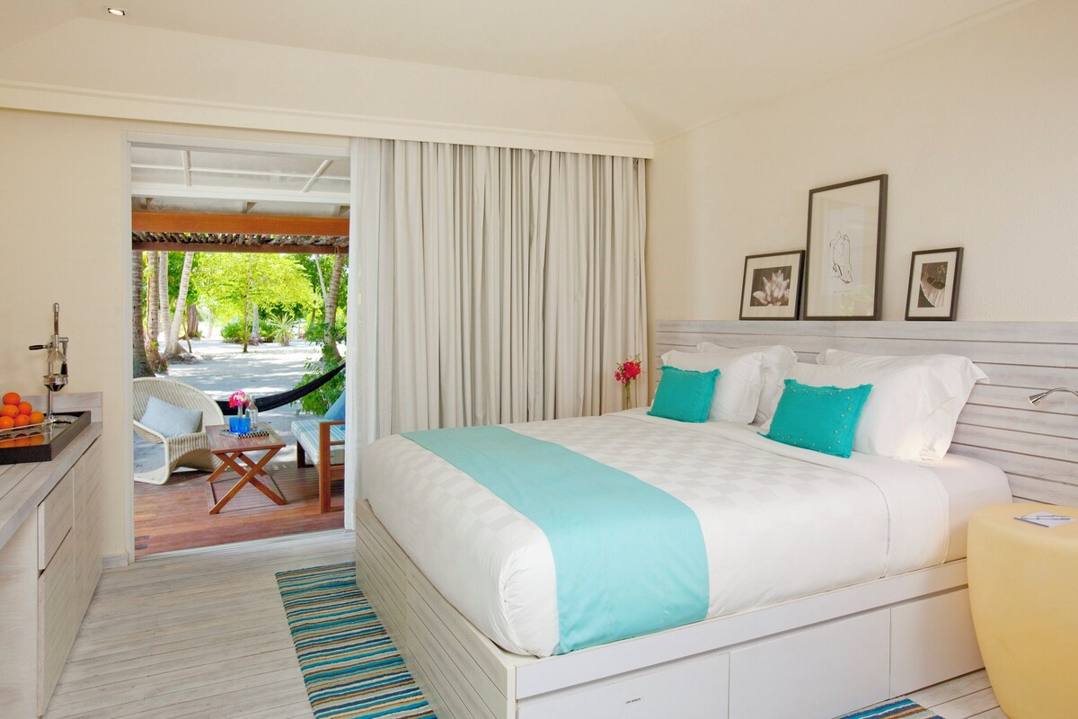 A bedroom with a large bed, a desk with a chair, and a view of a garden through a sliding door.