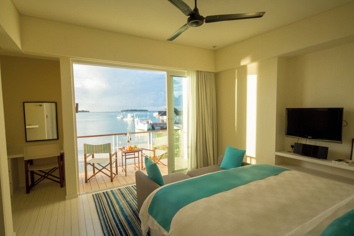 A hotel room with a balcony, a bed, a TV, and a desk.
