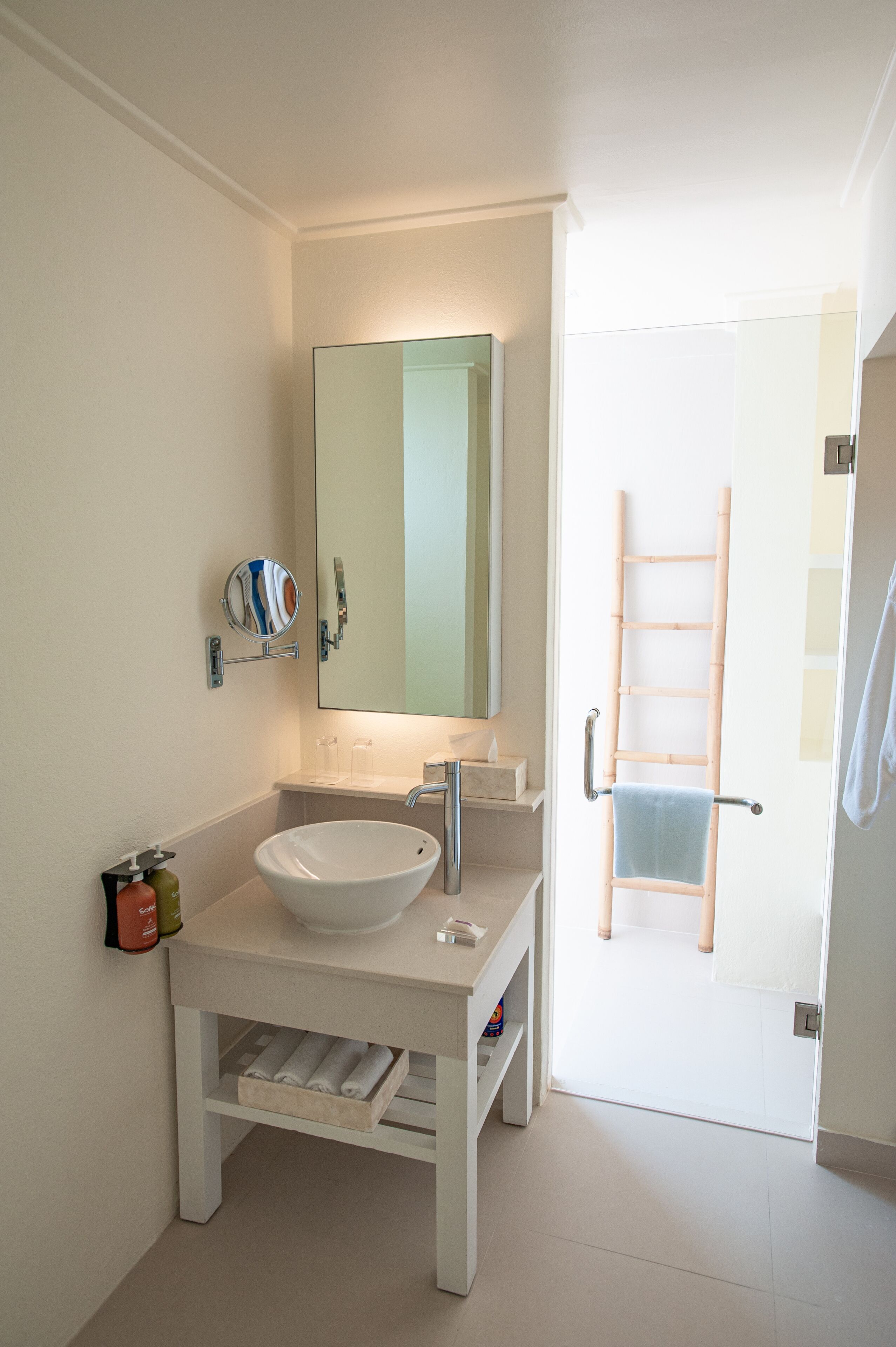 A bathroom with a white sink, mirror, and towel rack. There is a door leading to another room.