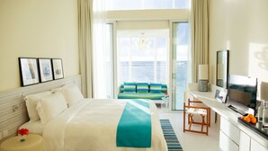 A hotel room with a bed, a desk with a TV, a chair, a small table with a vase, and a view of the sea through large windows. - Holiday Inn Resort Kandooma Maldives by IHG (Kandooma)