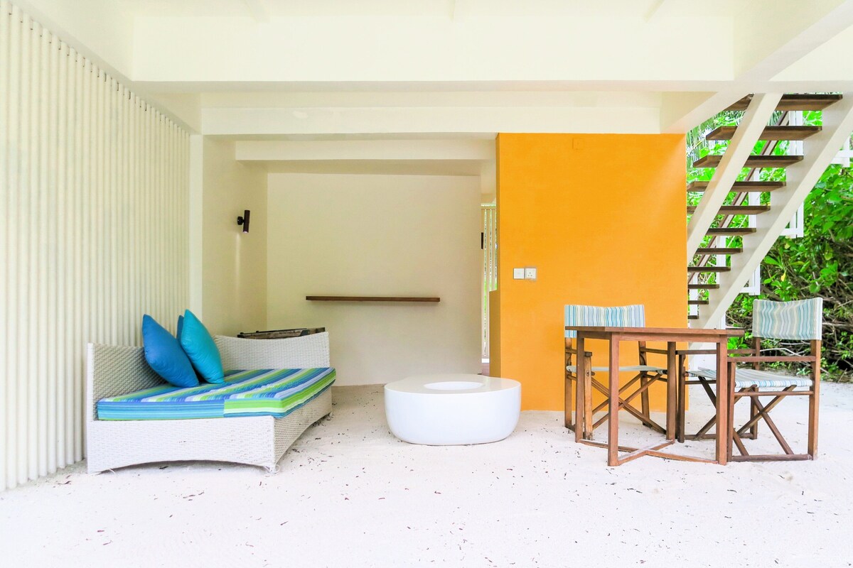 A modern outdoor seating area with a white sofa, blue cushions, and a round white ottoman. There is a wooden table with matching chairs.