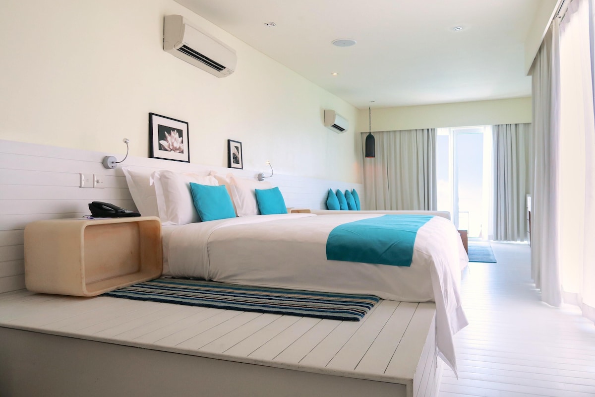 A modern hotel room with a large bed, a bedside table, and a view of the outdoors.