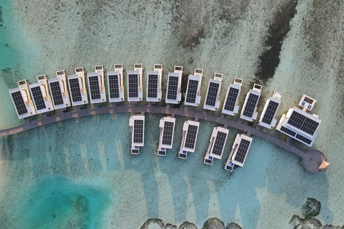 An aerial view of a resort with multiple buildings aligned along a curved shoreline, connected by a walkway.