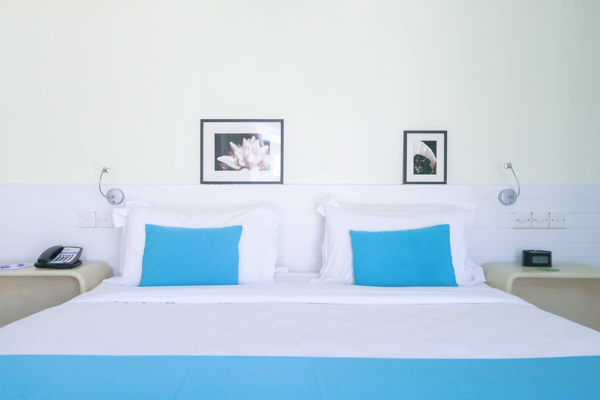 A hotel room with a bed, two bedside tables, a phone, and two framed pictures on the wall.