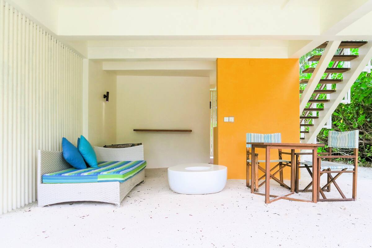 A modern outdoor seating area with a white sofa, blue cushions, and a round white ottoman. There is a wooden table with matching chairs.