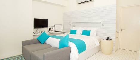 A modern bedroom with a bed, a grey sofa, a television, and a ceiling fan.