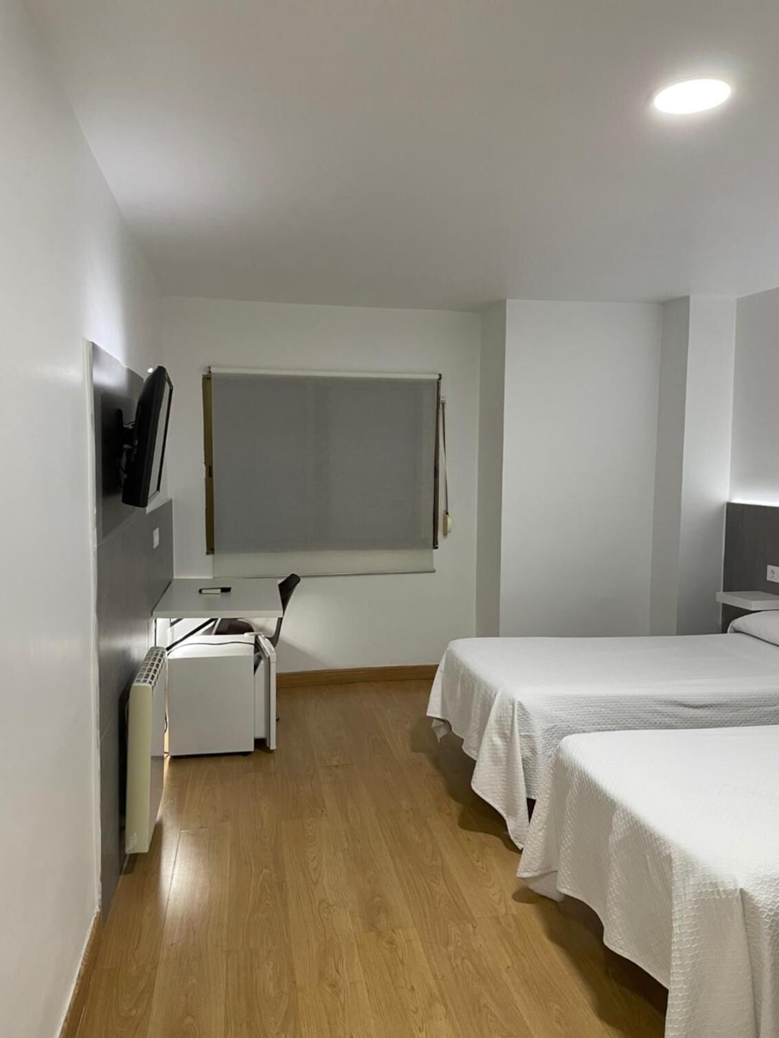 A small, clean room with a bed, a desk, and a window.