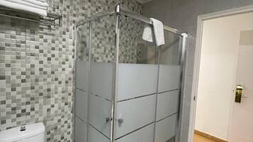 Un baño con ducha de vidrio, inodoro y pared con azulejos.