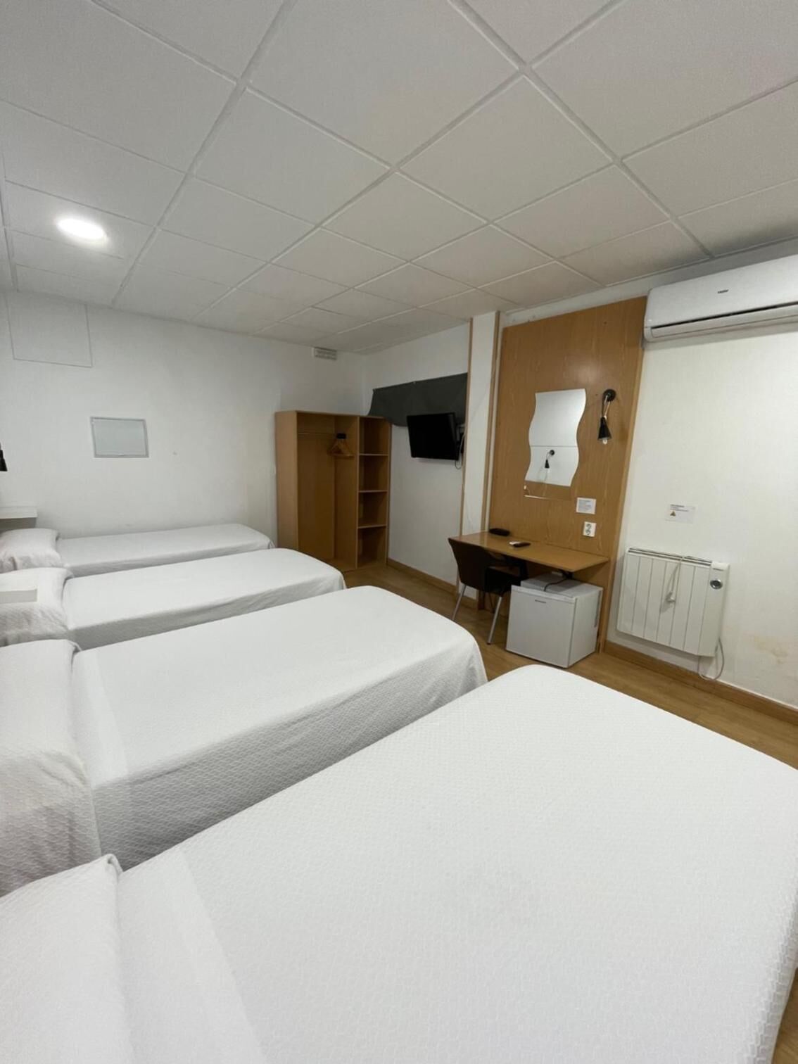 A hotel room with three beds, a desk, a chair, a television, and a wardrobe.