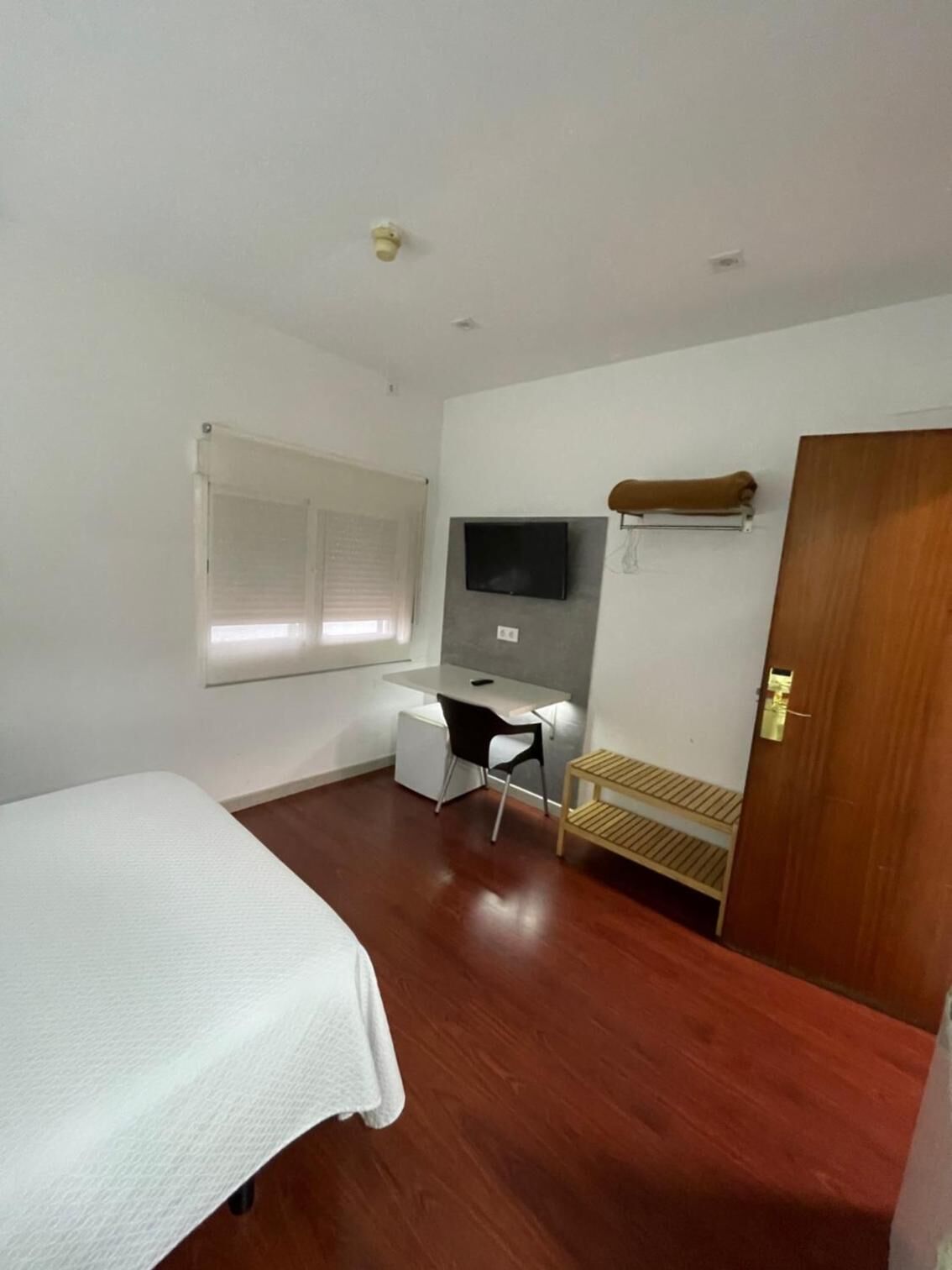 Une petite pièce propre, avec un lit, un bureau, une chaise, un téléviseur et une porte.