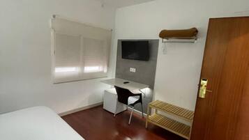 Una habitación pequeña y limpia con una cama, un escritorio, una silla, un televisor y una puerta.