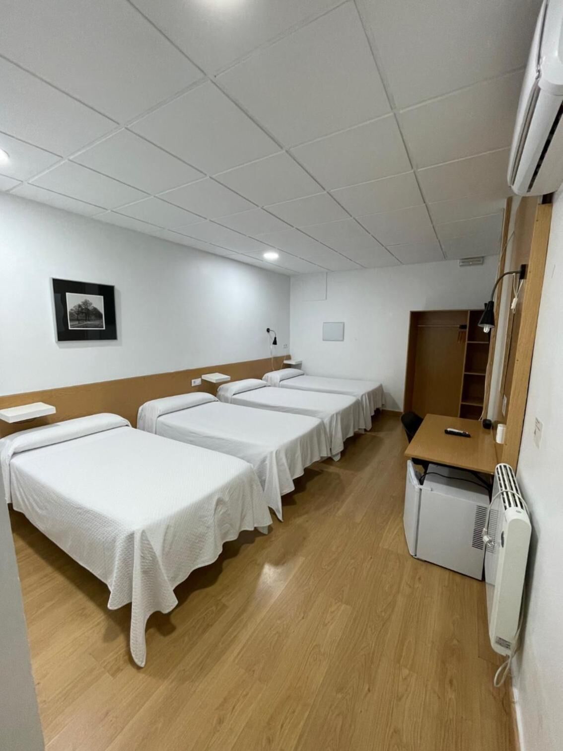 A hotel room with four single beds, a small desk, a chair, a heater, and a picture on the wall.