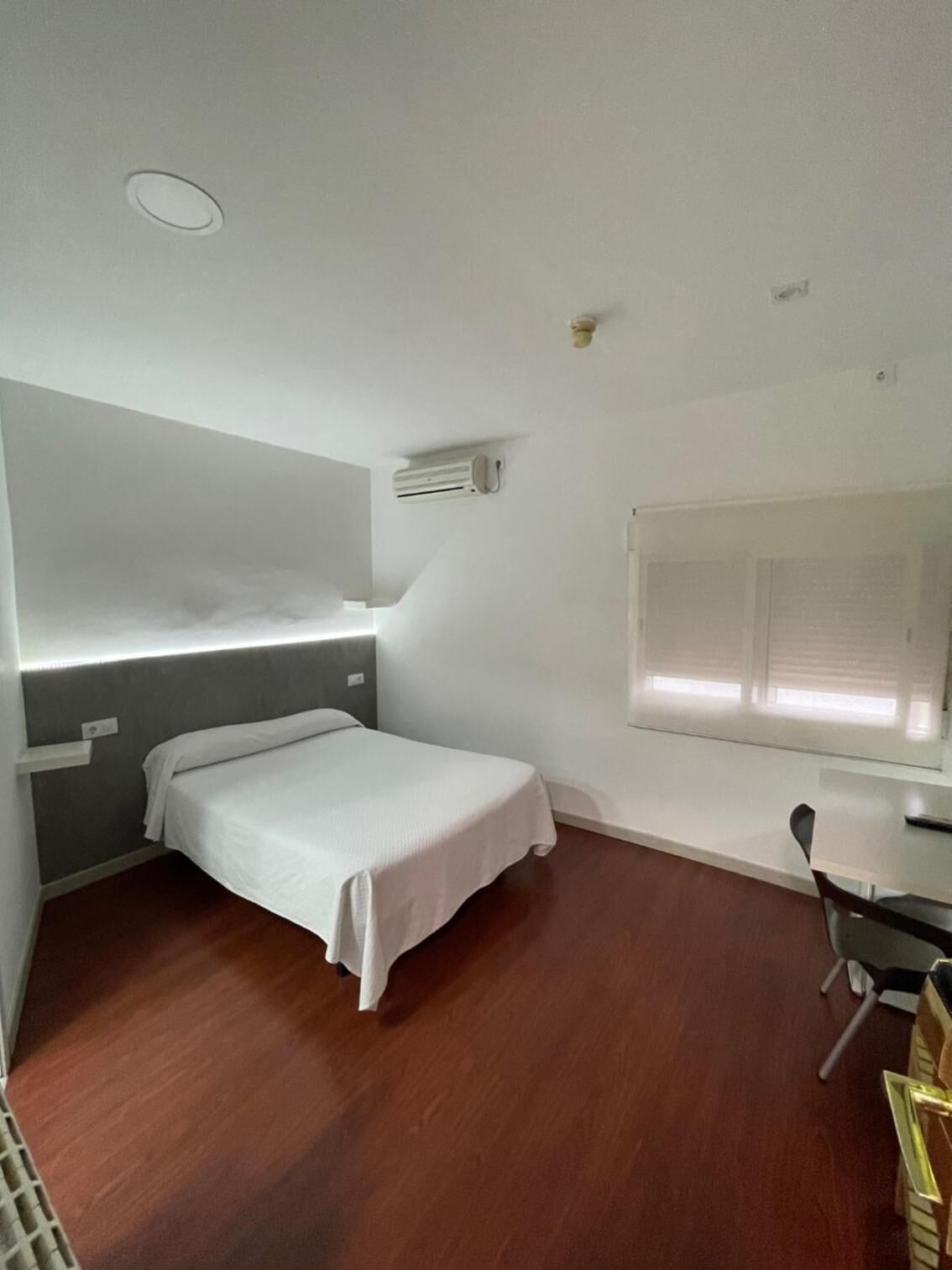 A small, modern room with a single bed, a desk, and a chair.