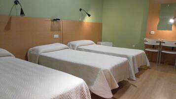 A room with three single beds, a desk, and two chairs.
