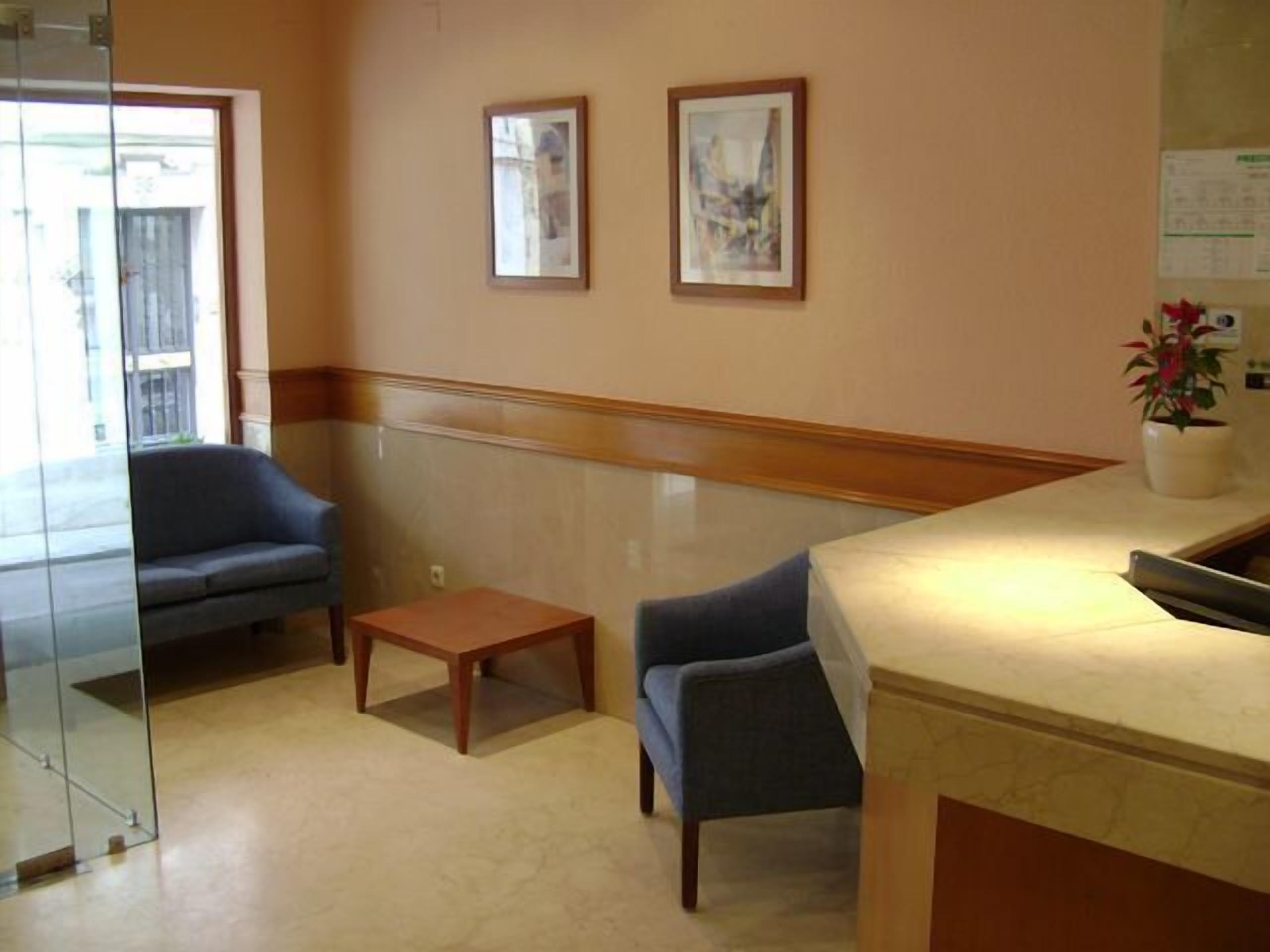 A reception area with a counter, two framed pictures on the wall, a small table, and two chairs.