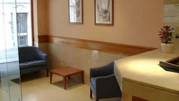 A reception area with a counter, two framed pictures on the wall, a small table, and two chairs.