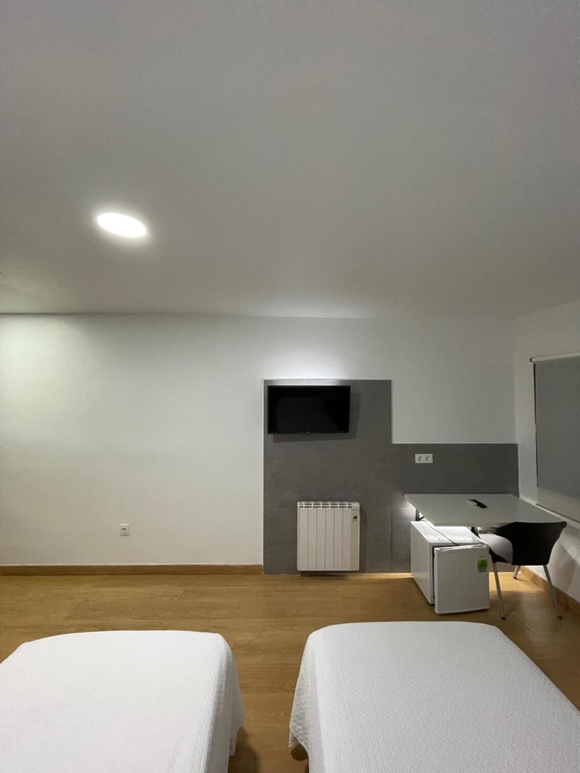 Habitación de hotel moderna con dos camas individuales, un pequeño rincón de cocina, un televisor de pantalla plana en la pared y un radiador.