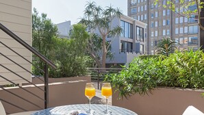 A round table with two glasses of orange juice and a magazine, set against a backdrop of a modern building and lush greenery. - Adderley Terraces J10 by CTHA (Cape Town)