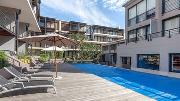Una piscina al aire libre, sombrillas, sillones reclinables de piscina