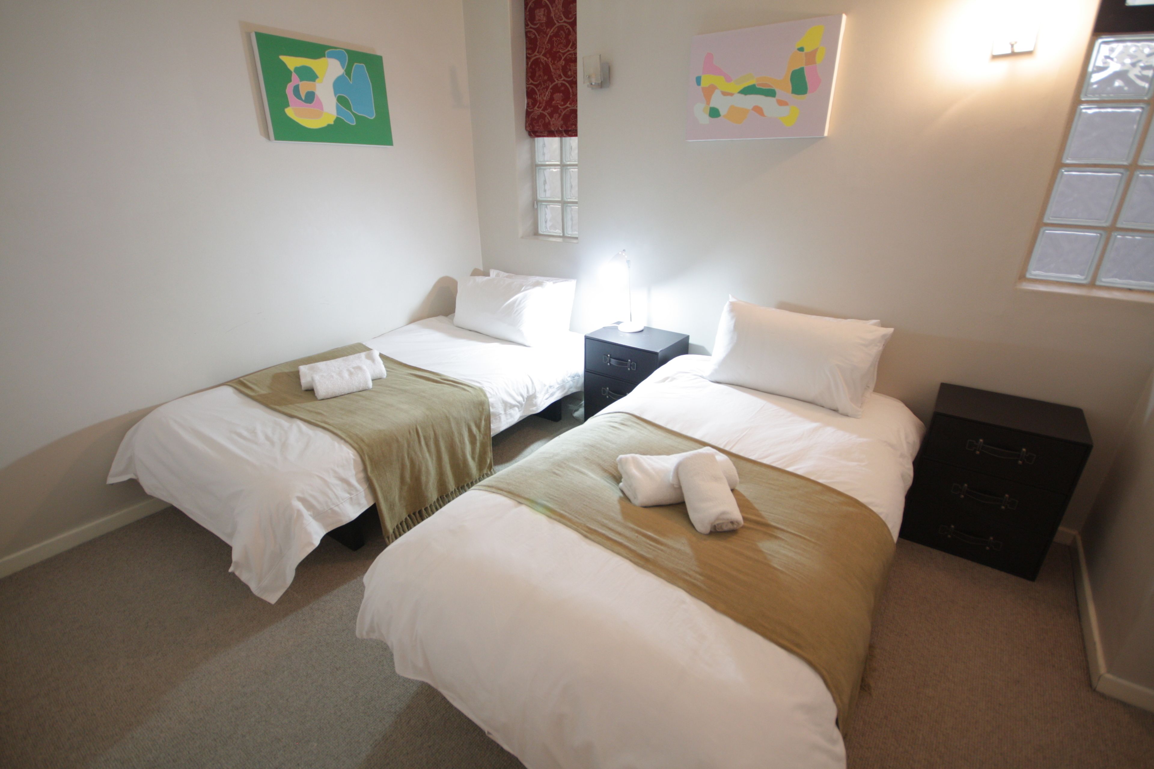 Een hotelkamer met twee bedden, een nachtkastje, een dressoir en kunstwerken aan de wand.
